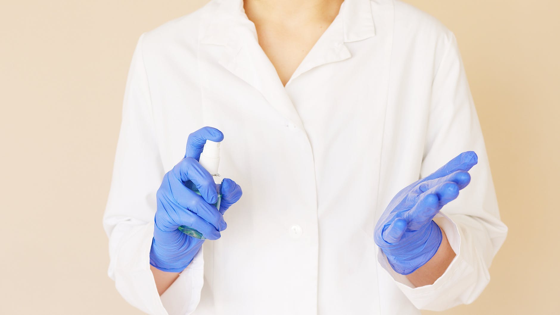 crop medical worker spraying sanitizer over hands in gloves