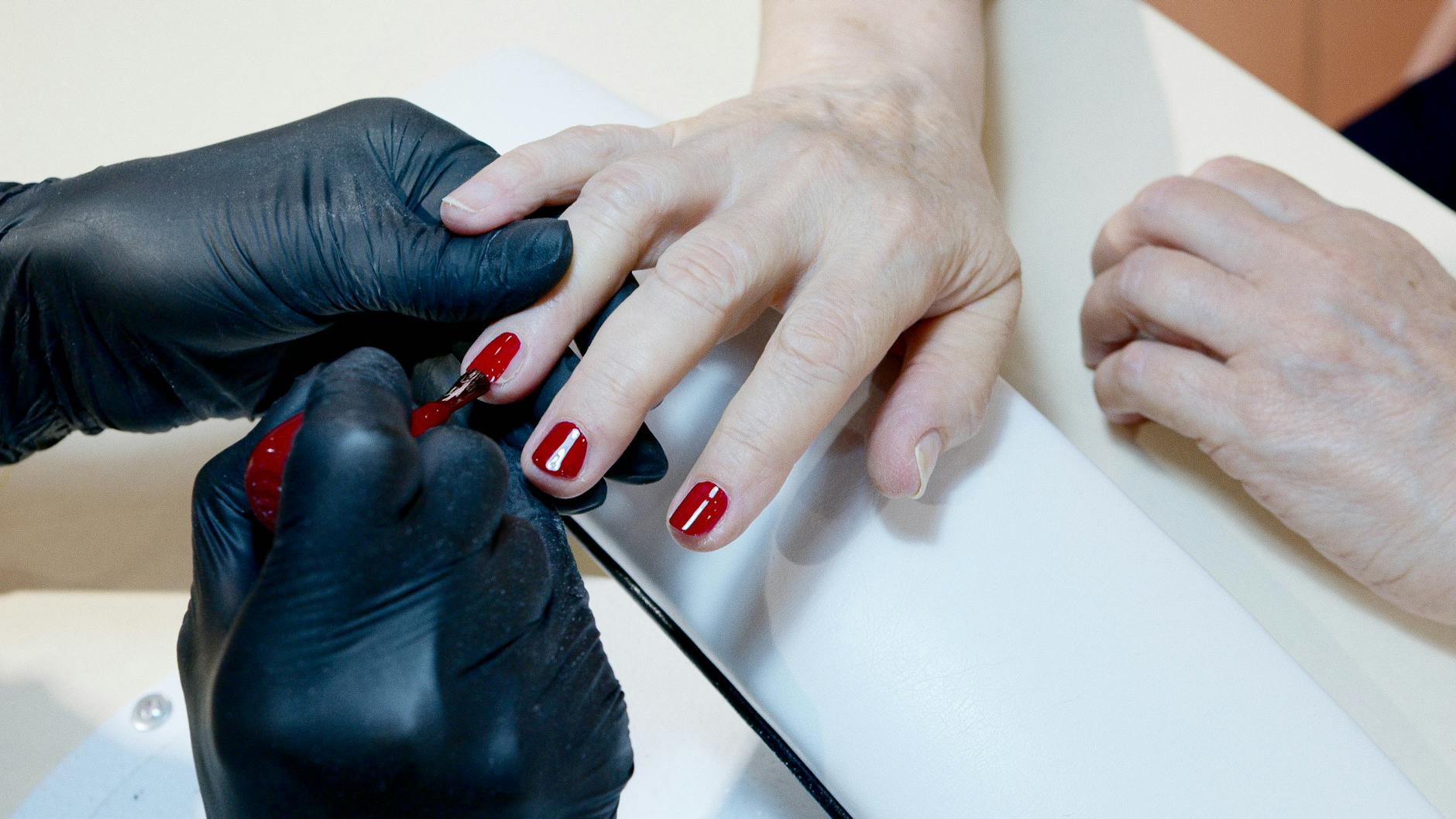 manicurist applying red nail polish on client
